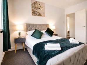 A hotel room with a large bed, two nightstands, a headboard, a painting, and a door.