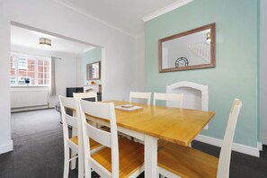 A dining area with a wooden table and white chairs, a fireplace, and a window with a view of a brick building.