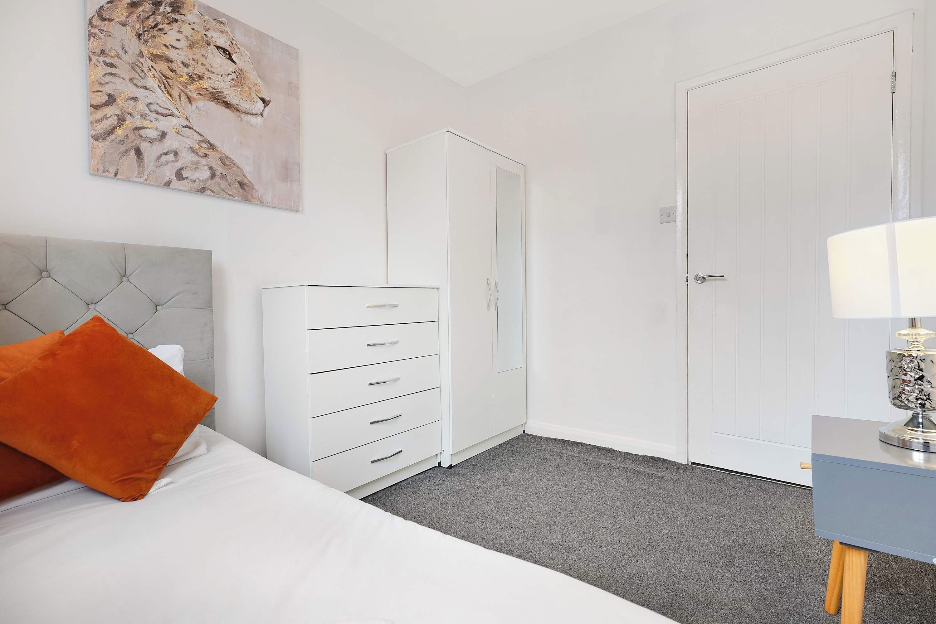 A bedroom with a bed, a dresser, a wardrobe, a nightstand, and a lamp.