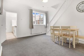A room with a staircase, a window with curtains, a radiator, and a wooden table with chairs.