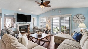 A living room with a fireplace, a ceiling fan, and a large clock on the wall. - 2706 W. 3rd St 2 Bedroom Home by RedAwning (Fernandina Beach)