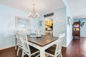 A dining area with a wooden table and white chairs, a chandelier, and a sign that reads 'The Beach Solves everything.' - 2706 W. 3rd St 2 Bedroom Home by RedAwning (Fernandina Beach)