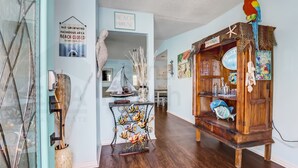 A beach-themed interior with a wooden bookshelf, a parrot decoration, and a sailboat model. - 2706 W. 3rd St 2 Bedroom Home by RedAwning (Fernandina Beach)