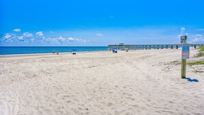 A beach with a pier extending into the ocean, a signpost with route information, and a clear blue sky. - 8 Sea Castles 3 Bedroom Condo by RedAwning (Fernandina Beach)