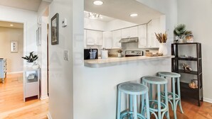 A modern kitchen with white cabinets, a stainless steel range hood, and a countertop with bar stools. - 8 Sea Castles 3 Bedroom Condo by RedAwning (Fernandina Beach)