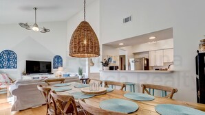 A modern kitchen with white cabinets, a central island, and a dining area with a wooden table and chairs. - 8 Sea Castles 3 Bedroom Condo by RedAwning (Fernandina Beach)