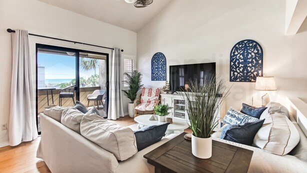 A modern living room with a sofa, coffee table, and TV. There is a balcony with a view. - 8 Sea Castles 3 Bedroom Condo by RedAwning (Fernandina Beach)