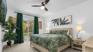 Ein Schlafzimmer mit einem Bett, einem Nachttisch, einem Deckenventilator, einem großen Fenster mit Vorhängen und einer Topfpflanze.