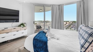 Une chambre d’hôtel moderne dotée d’un grand lit, d’un téléviseur fixé au mur, d’un balcon offrant une vue sur la ville et d’une commode en bois.