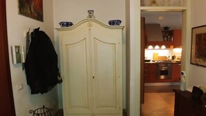 Un couloir avec une armoire blanche, un tapis à motifs et une cuisine visible au fond.
