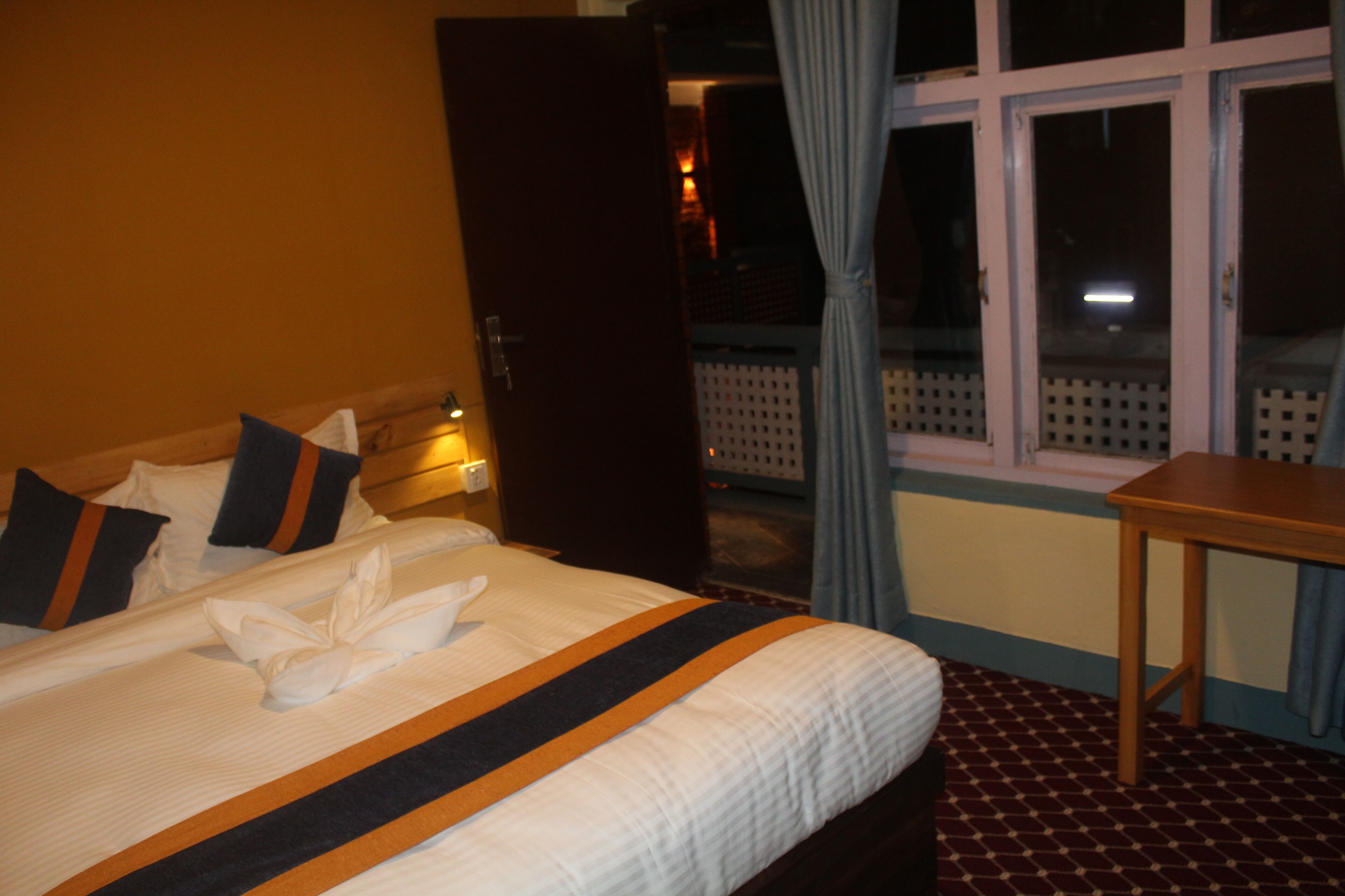 A hotel room with a neatly made bed, a wooden nightstand, and a window with curtains.