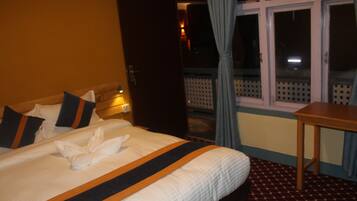 A hotel room with a neatly made bed, a wooden nightstand, and a window with curtains.