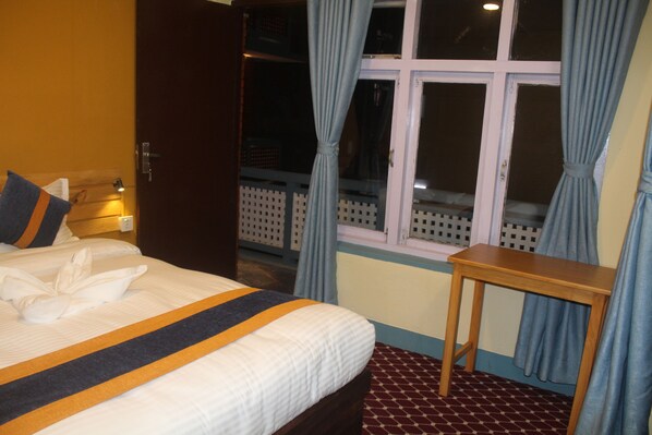 Una habitación de hotel con una cama, una mesita de noche de madera y una ventana con cortinas.