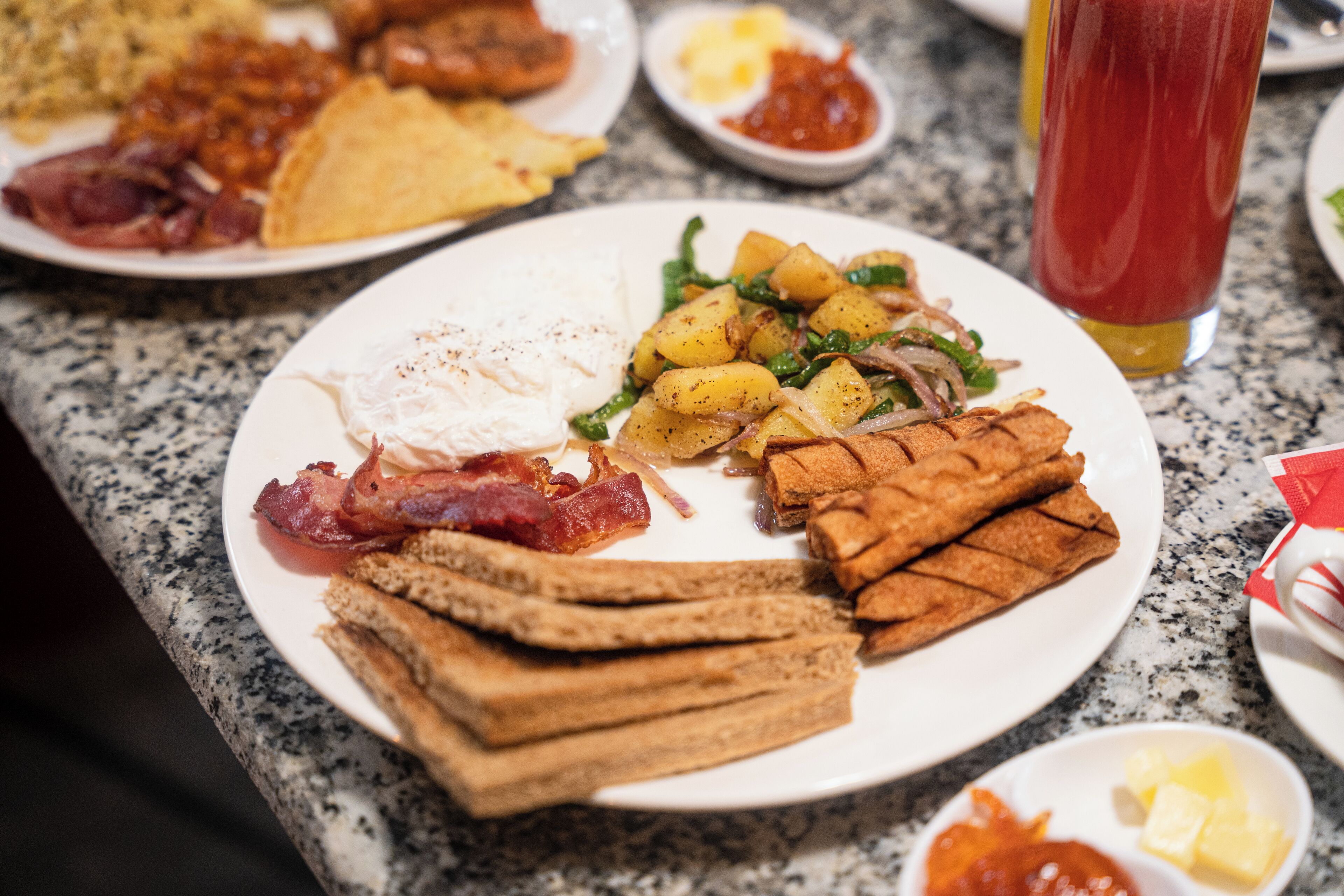 A breakfast plate with bacon, eggs, toast, potatoes, and greens.