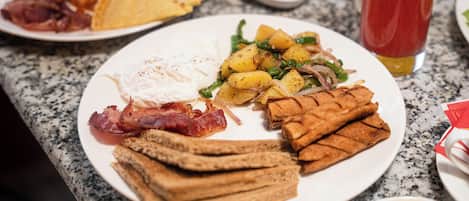 Un plato de desayuno con tocino, huevos, tostadas, papas y vegetales verdes.
