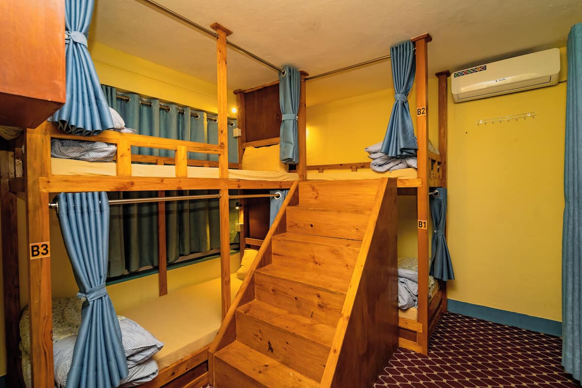 Ein Schlafsaalzimmer mit Etagenbetten, einer Holztreppe und einer Klimaanlage.
