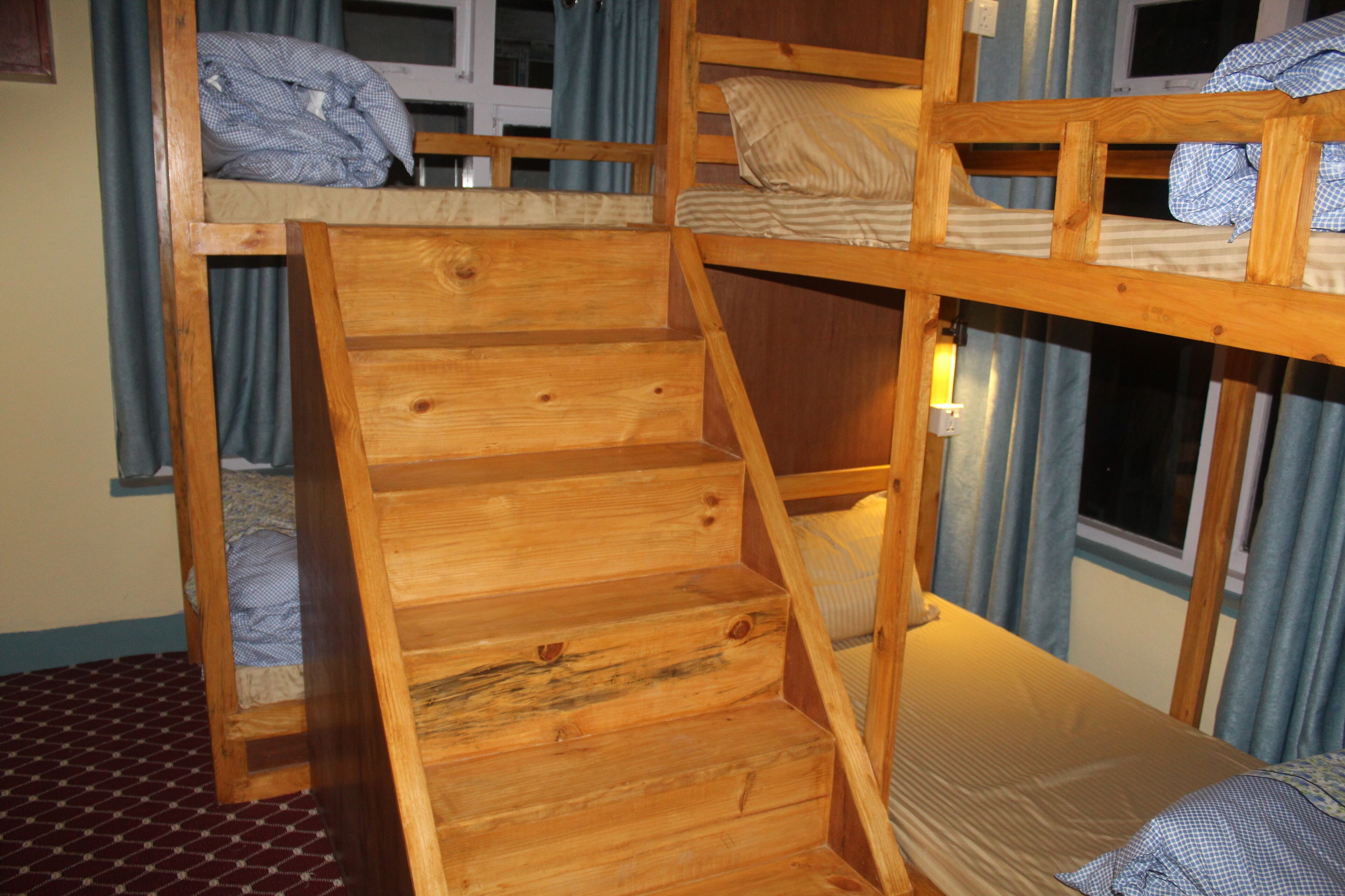 A bunk bed room with a wooden ladder, a window with curtains, and a bed with a striped pillow.