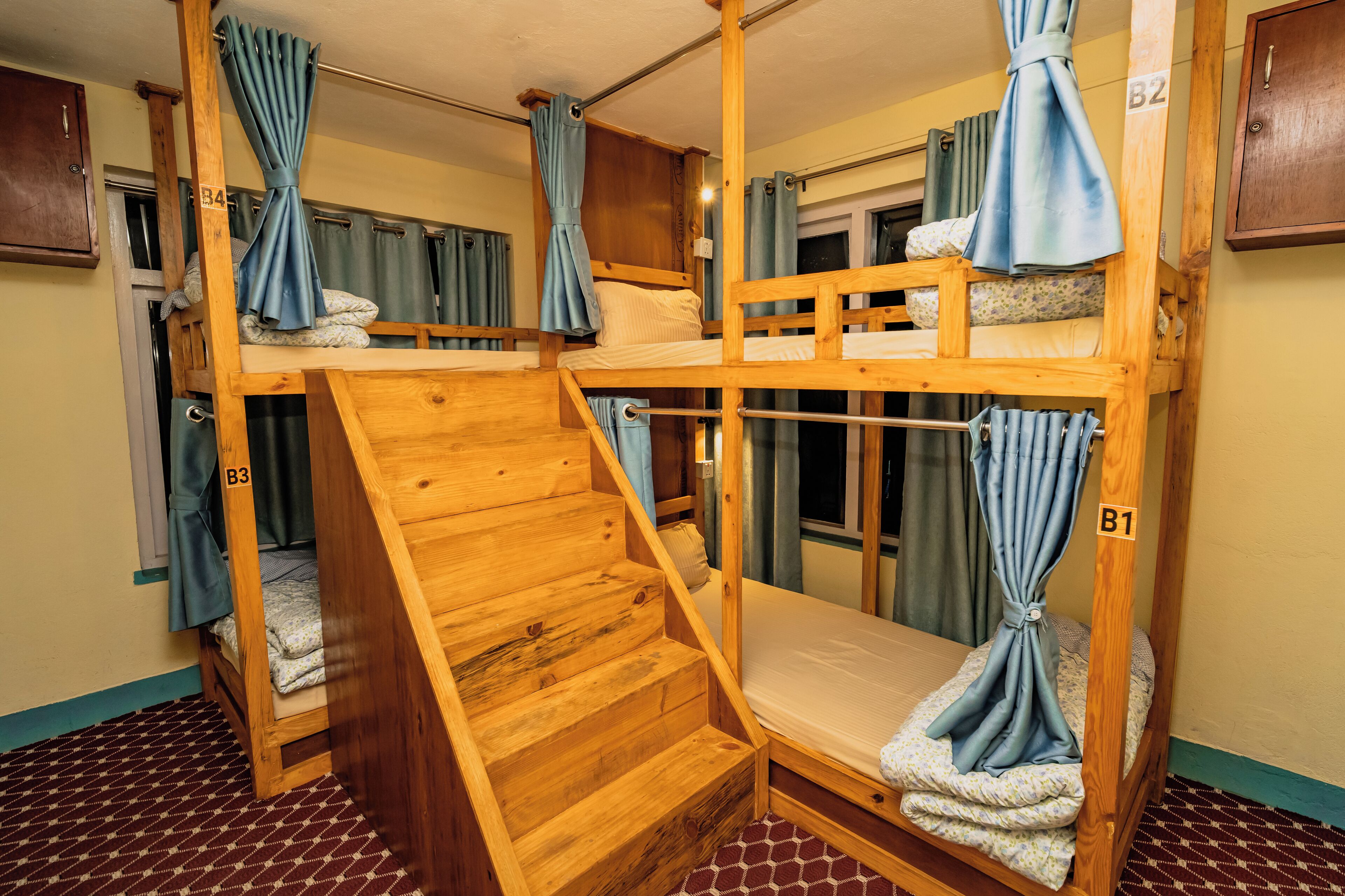 Habitación con literas de madera, una pequeña escalera y cortinas en las ventanas.