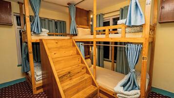 Habitación con literas de madera, una pequeña escalera y cortinas en las ventanas.