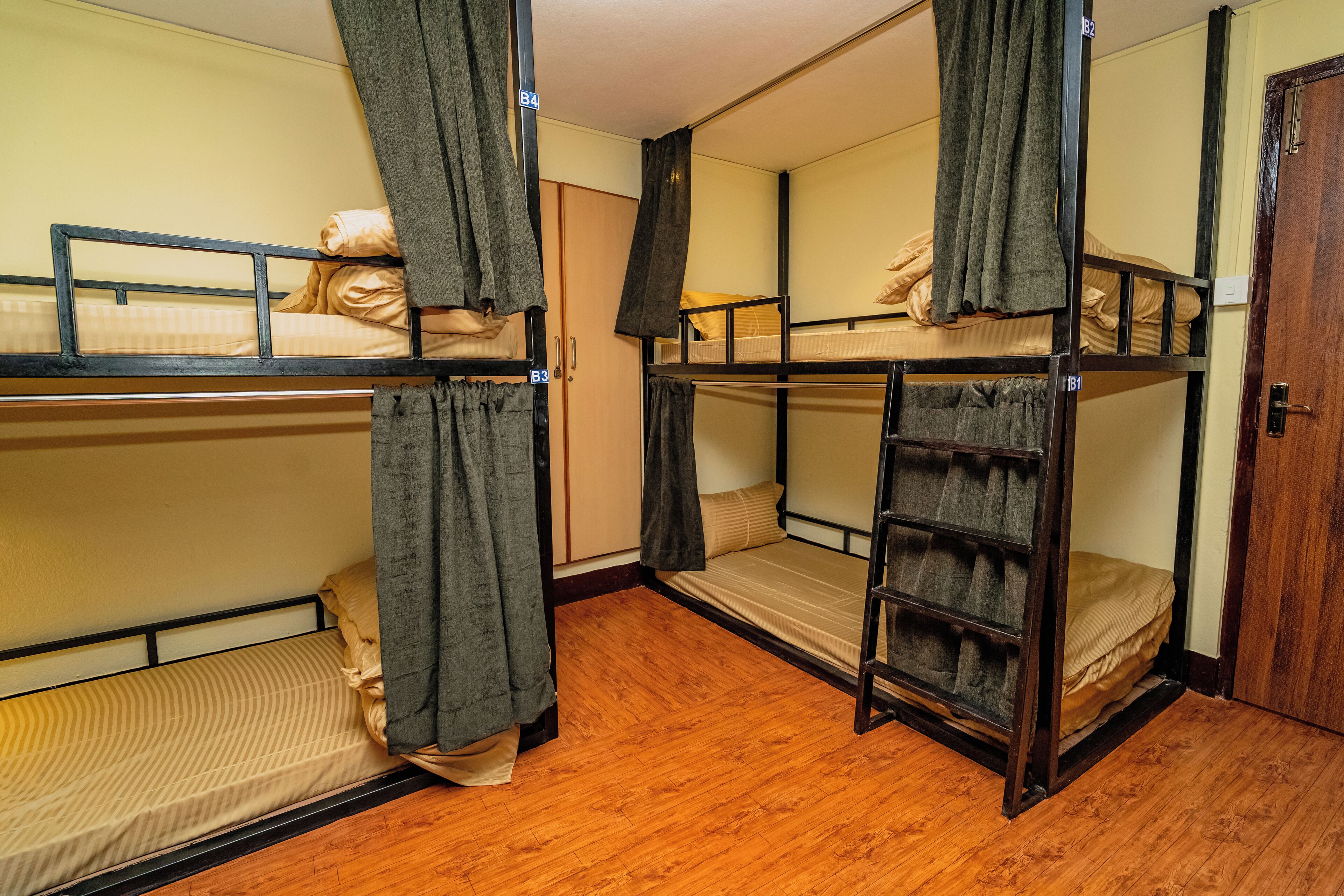 A dormitory room with bunk beds, wooden flooring, and curtains.