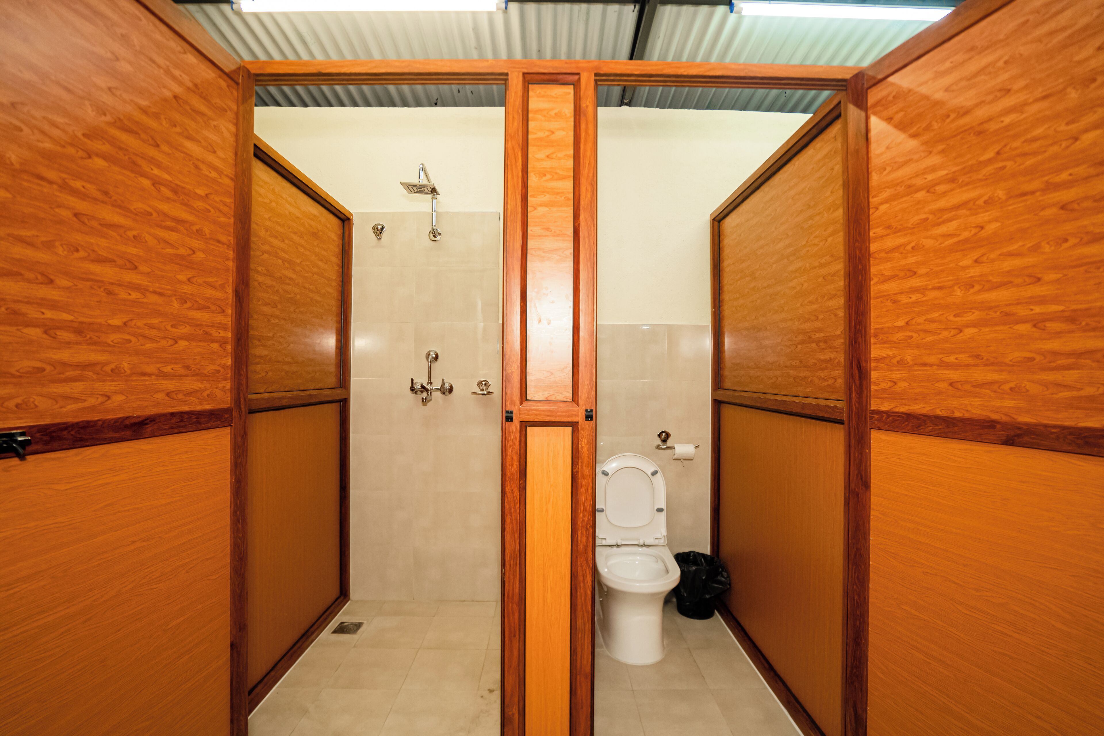 Une salle de bain aux murs lambrissés, équipée de toilettes, d’une douche et d’une poubelle.
