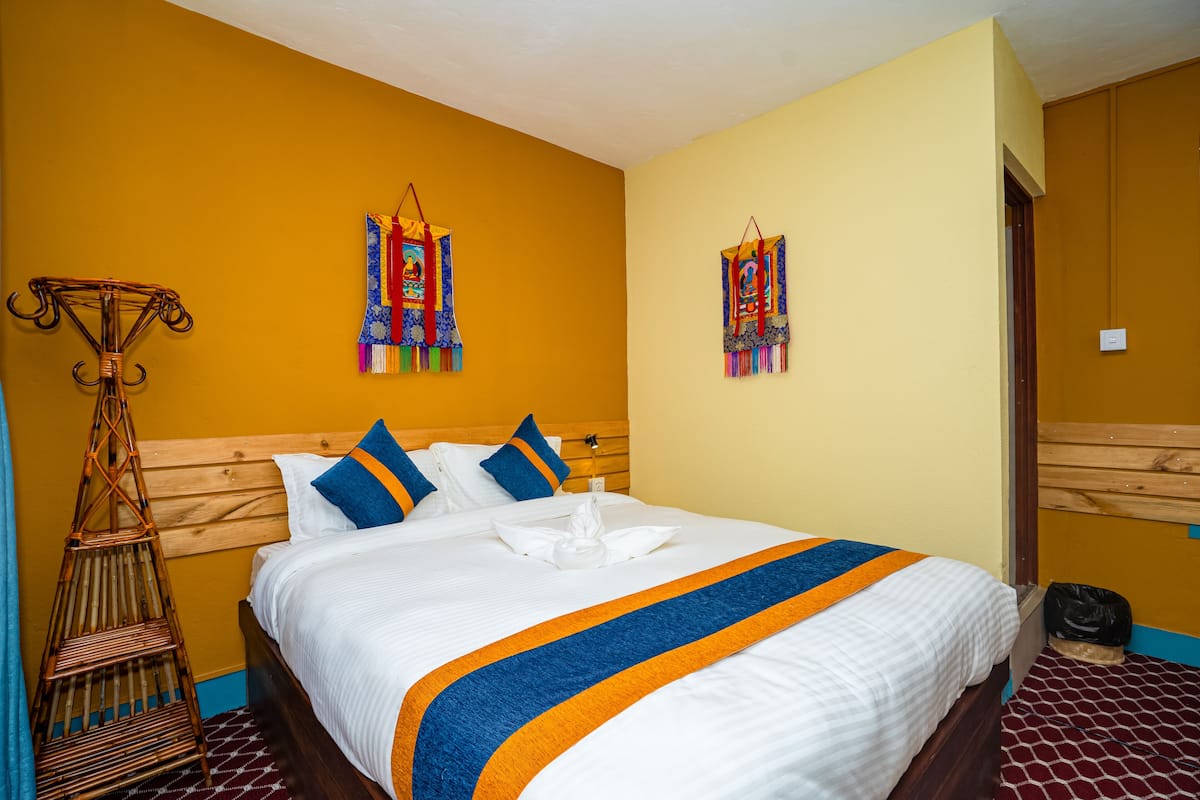 Ein Hotelzimmer mit Holz-Kopfteil, einem Bett mit weißer Bettwäsche und blau-orangen Akzenten sowie zwei Wanddekorationen.