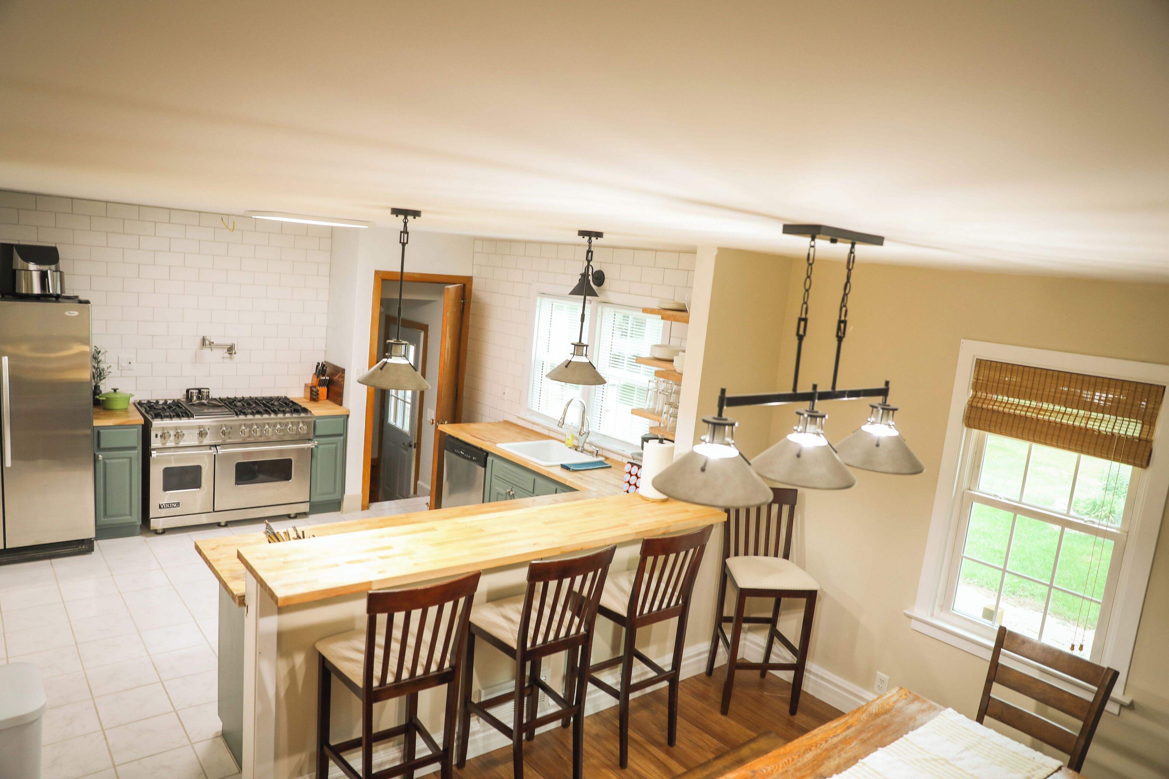 A kitchen with a wooden island, bar stools, a stove, and pendant lights.