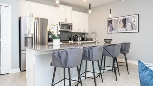 Una cucina moderna con mobili bianchi, elettrodomestici in acciaio inossidabile e un'isola centrale con sgabelli da bar.