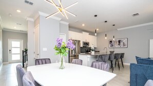 Una cucina moderna con mobili bianchi, elettrodomestici in acciaio inossidabile e un'area pranzo con tavolo bianco e sedie grigie.