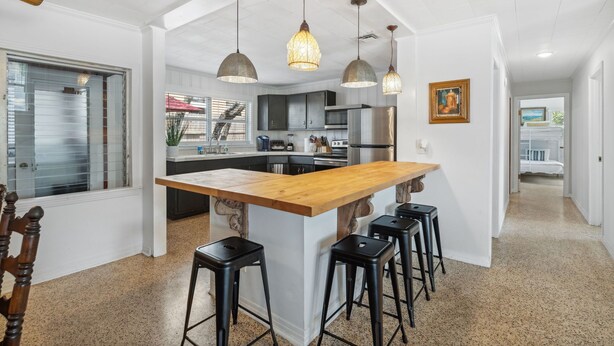 Una cocina moderna con una isla central, iluminación colgante y vista al área de comedor.