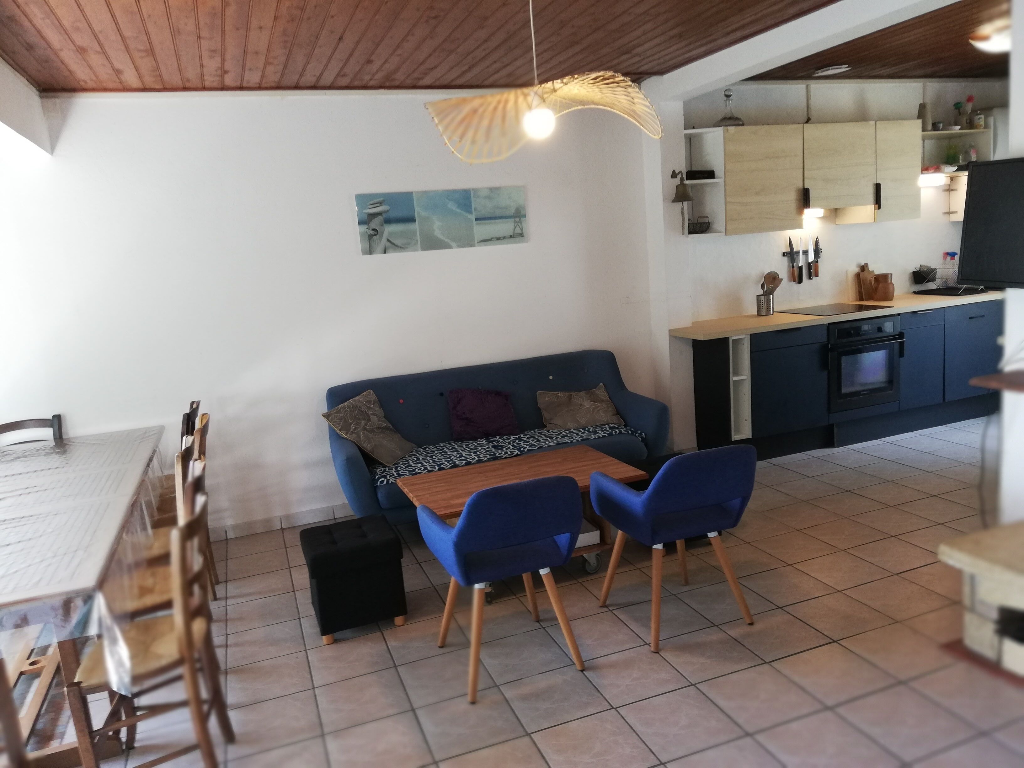 A dining area with a table, chairs, and a sofa. There is a kitchen area with cabinets and a stove.
