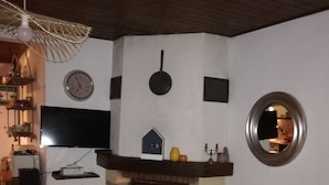 Un soggiorno con camino, due poltrone blu, una televisione e un orologio appeso al muro.