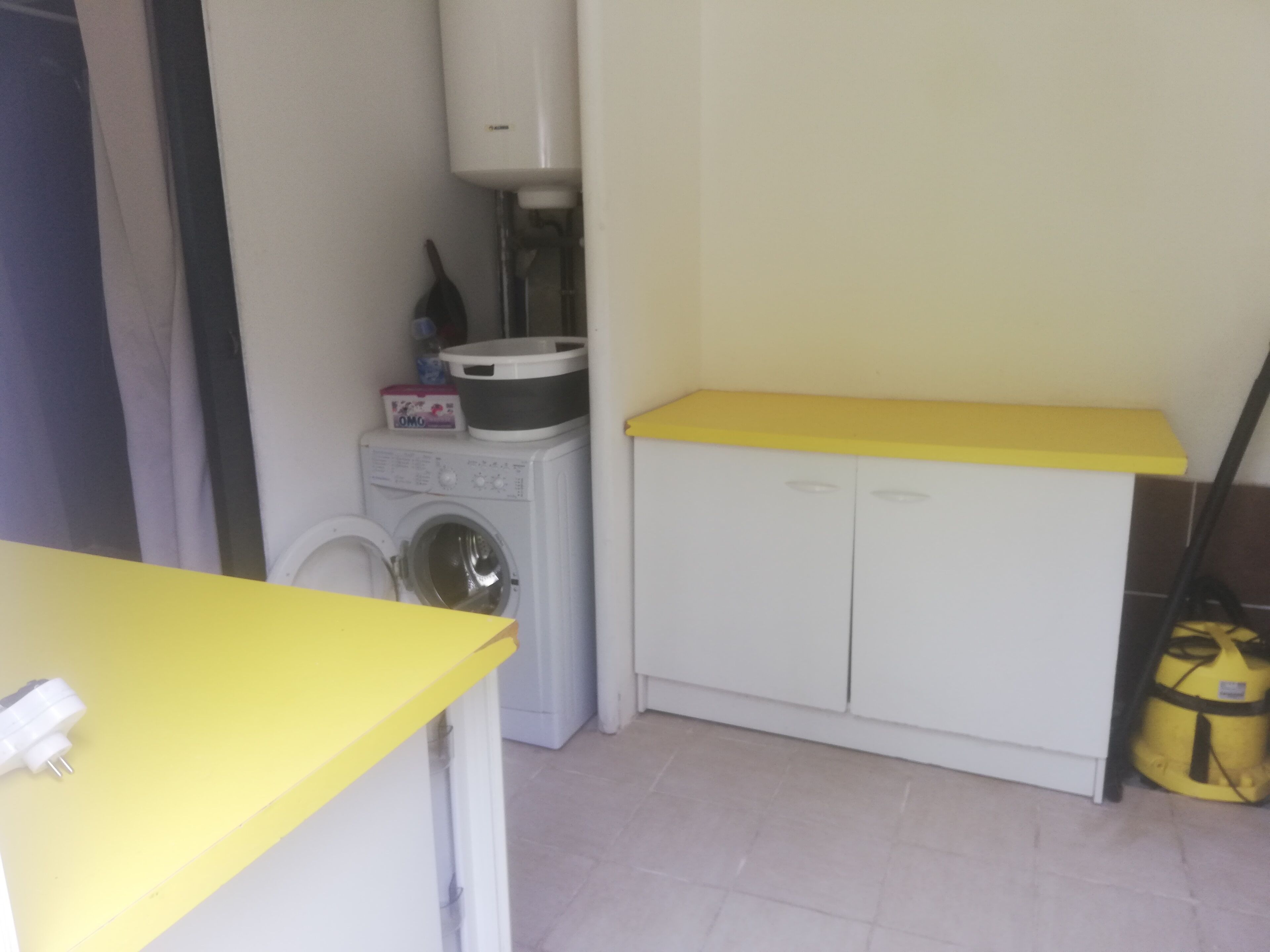 A compact laundry area with a washing machine, a drying machine, and a small cabinet with a yellow countertop.
