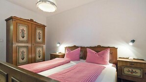 Una cama doble con ropa de cama rosa a cuadros, dos mesitas de noche con lámparas y un armario de madera con diseños florales.