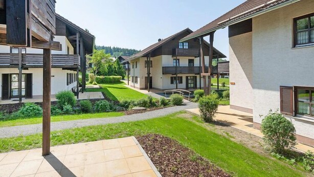 Un complejo residencial de arquitectura moderna, con varias casas de dos pisos y balcones, un césped bien cuidado y cielo despejado.