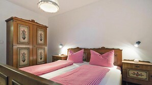 Een tweepersoonsbed met een geruit beddegoed, twee nachtkastjes met lampen, een houten garderobe met bloemenmotieven en een kroonluchter.