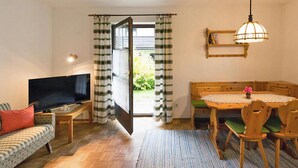 Een woonkamer met een televisie, bank en een eettafel met stoelen.