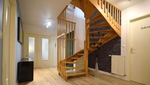 Un escalier avec des rampes en bois mène au deuxième étage. Une console noire est adossée au mur, à gauche.