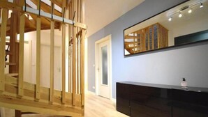 Une pièce avec un escalier en bois, une coiffeuse noire et un grand miroir qui reflète l’escalier.