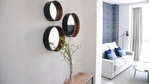 A modern living room with a white sofa, blue cushions, a coffee table, and a vase with green branches. Three round mirrors are mounted on the wall. - Capuchinos Cathedral (Málaga)