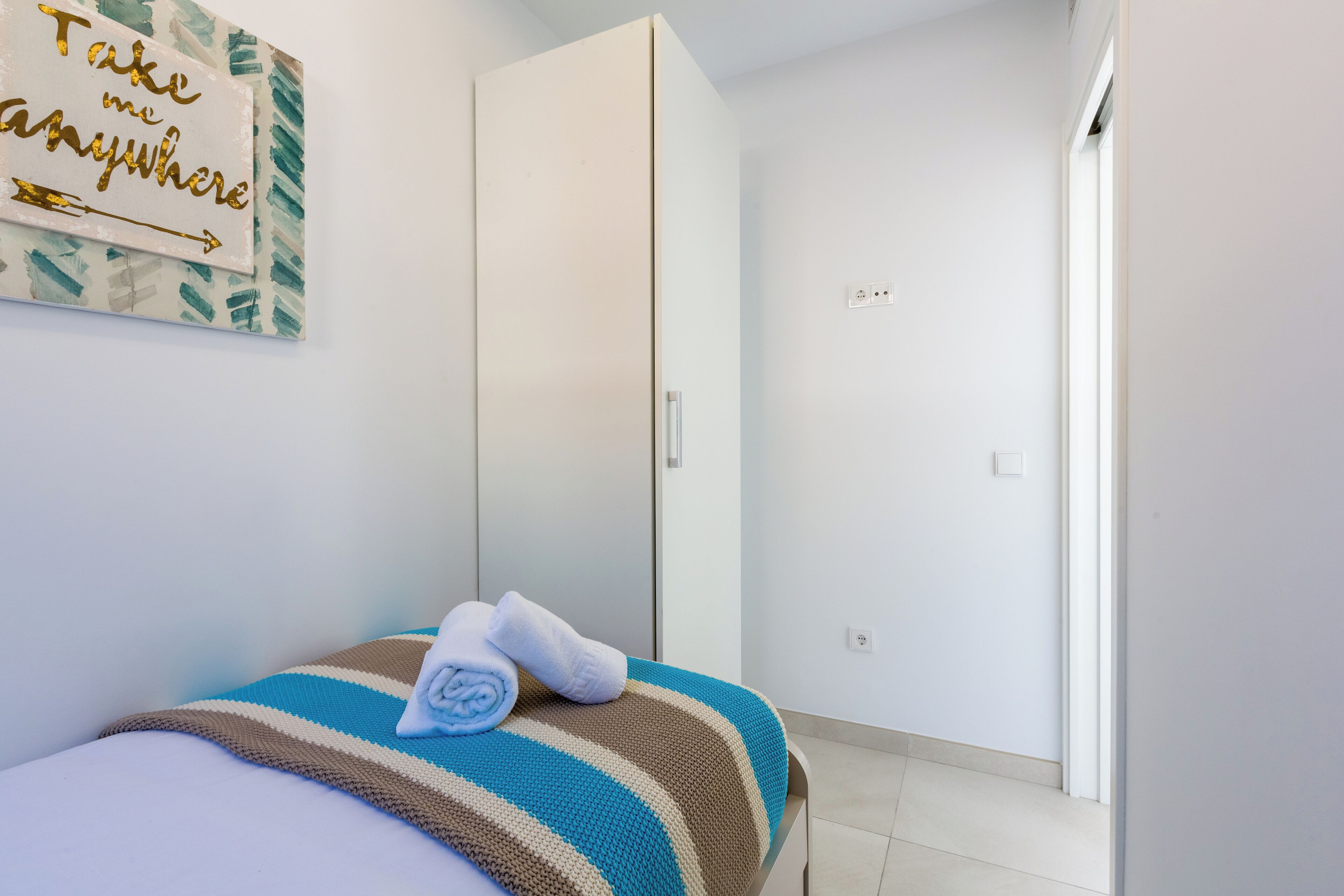 Un dormitorio con cama, armario, toalla y una cita motivacional en la pared.