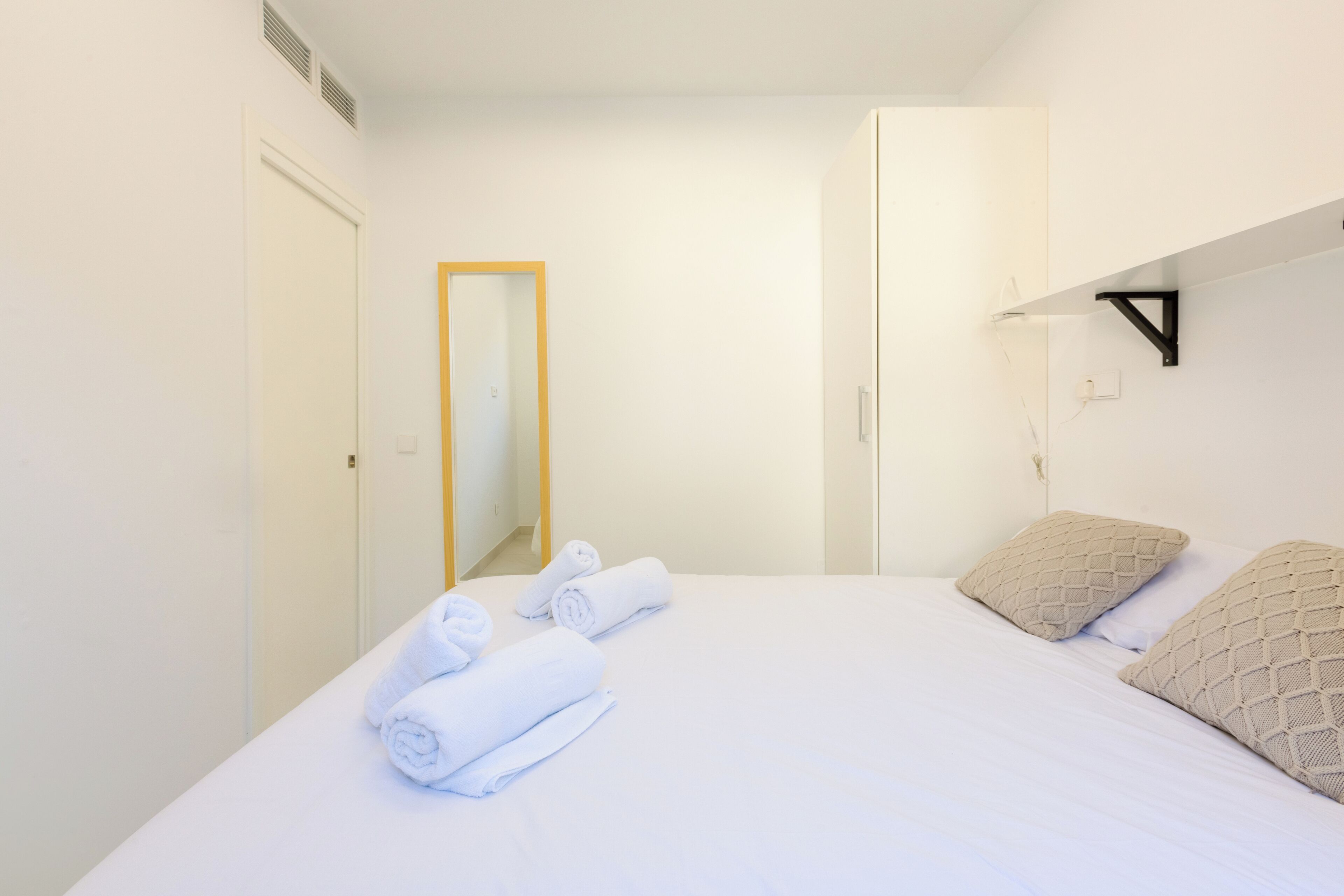A hotel room with a neatly made bed, a wardrobe, and a mirror.