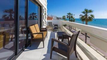 Een balkon met stoelen en een tafel, met uitzicht op een strand met palmbomen en de zee.