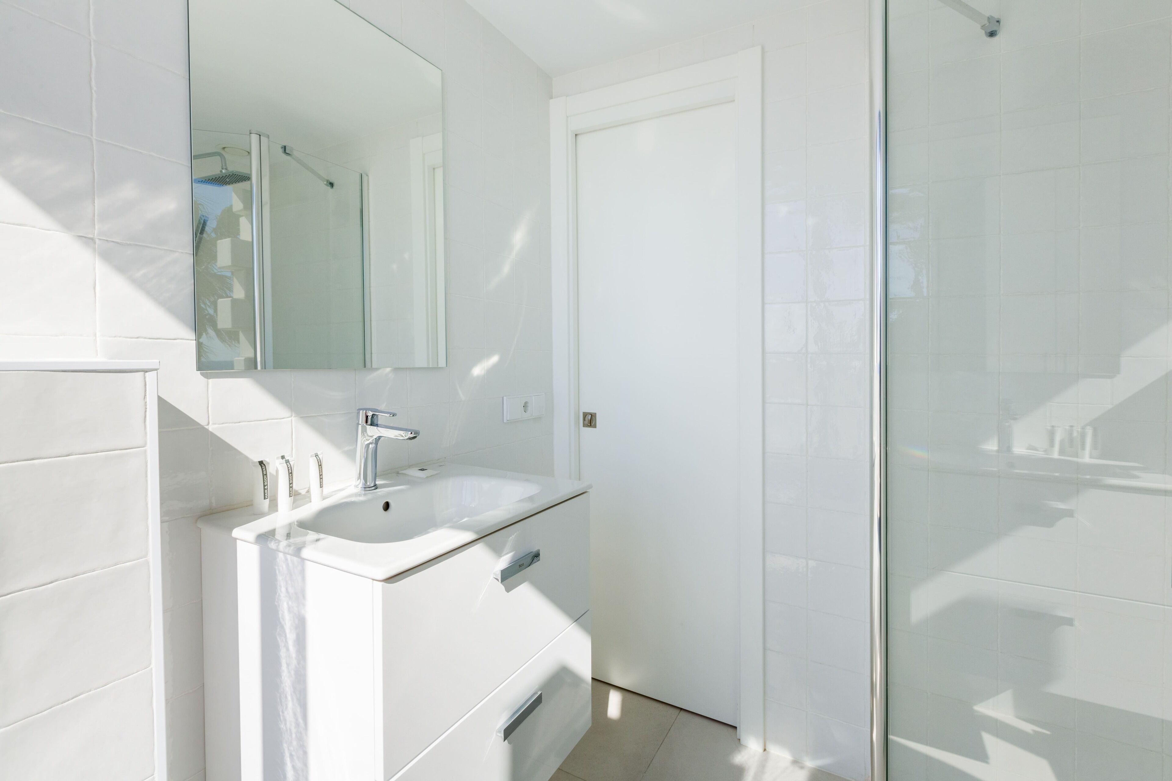 A modern bathroom with a white sink, mirror, and glass shower enclosure.