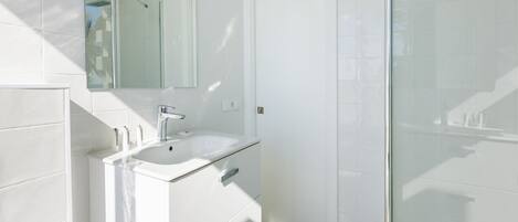 A modern bathroom with a white sink, mirror, and glass shower enclosure.