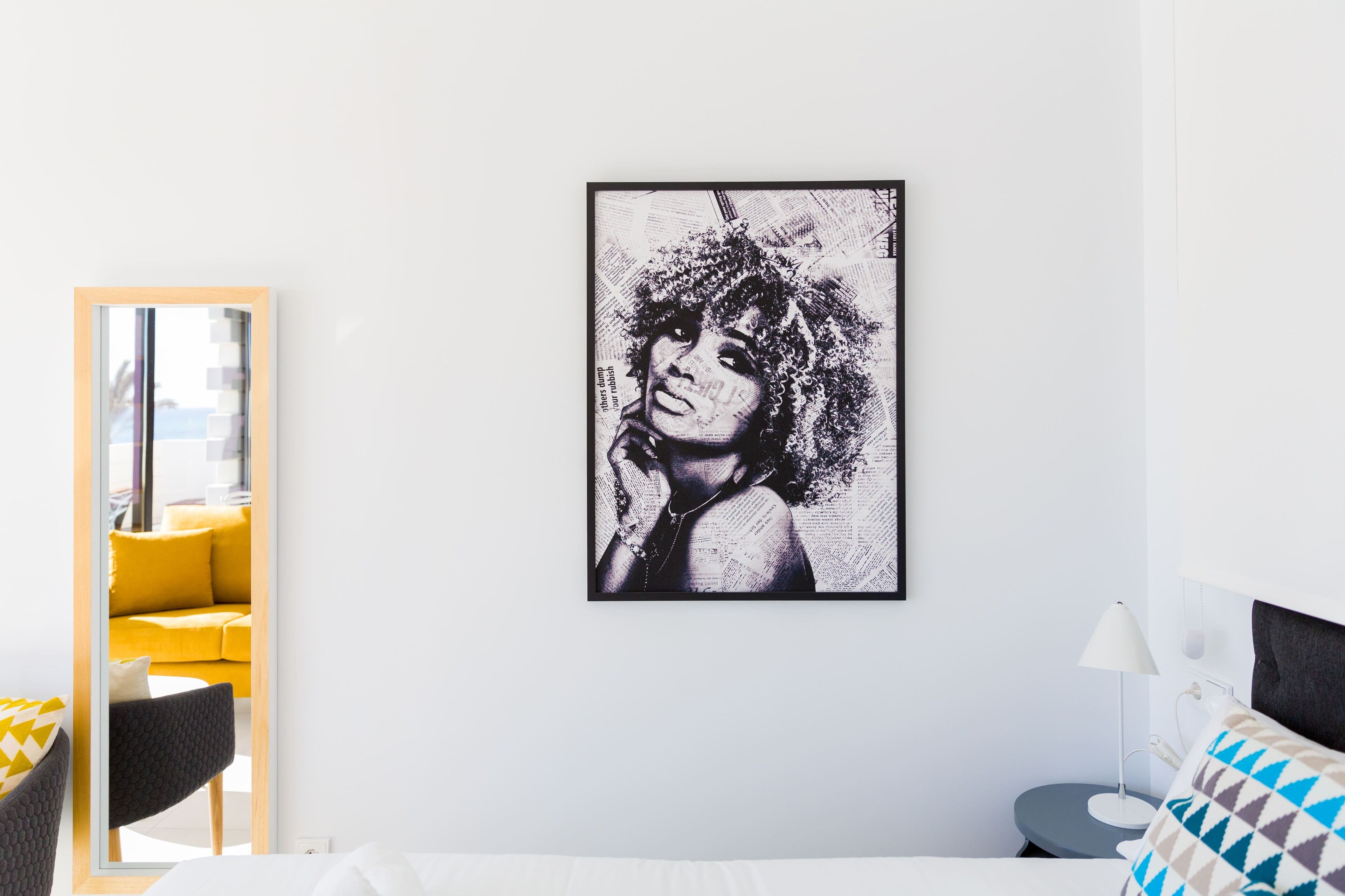 Un hotel moderno con un espejo grande, una cama con almohadas estampadas y una obra de arte enmarcada en la pared.