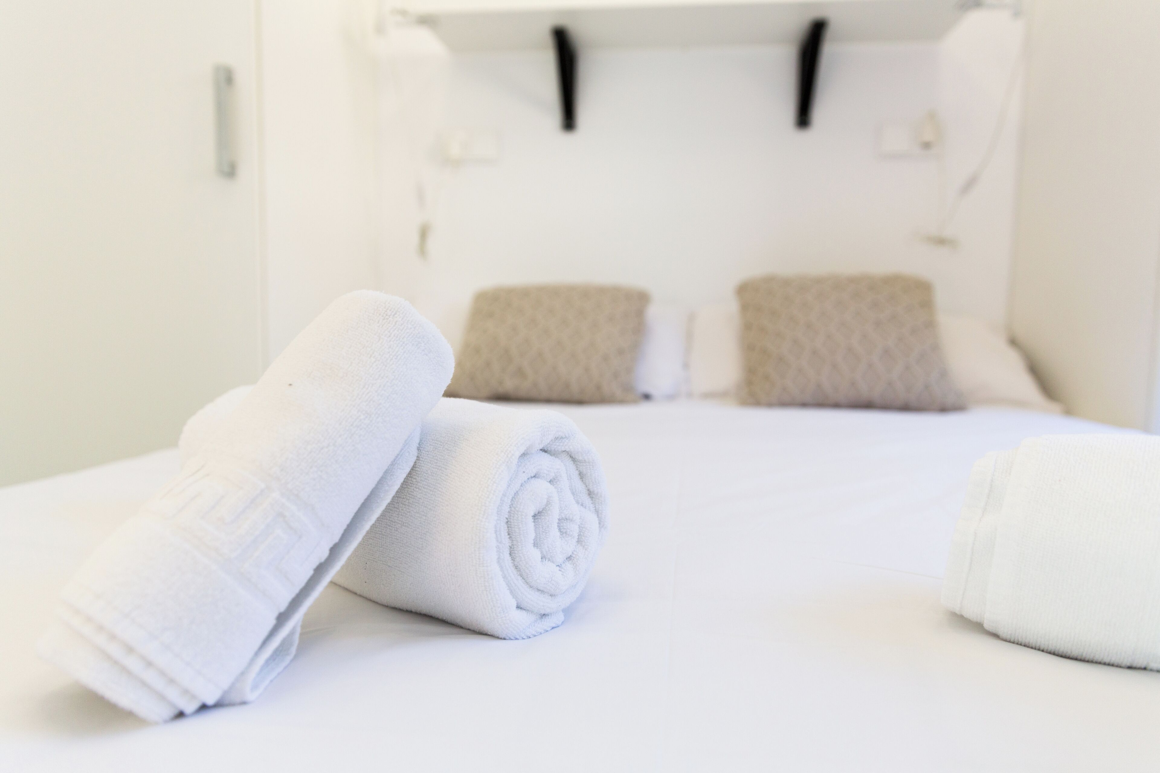 Una cama bien hecha con almohadas blancas y beige, y toallas blancas enrolladas sobre la cama.