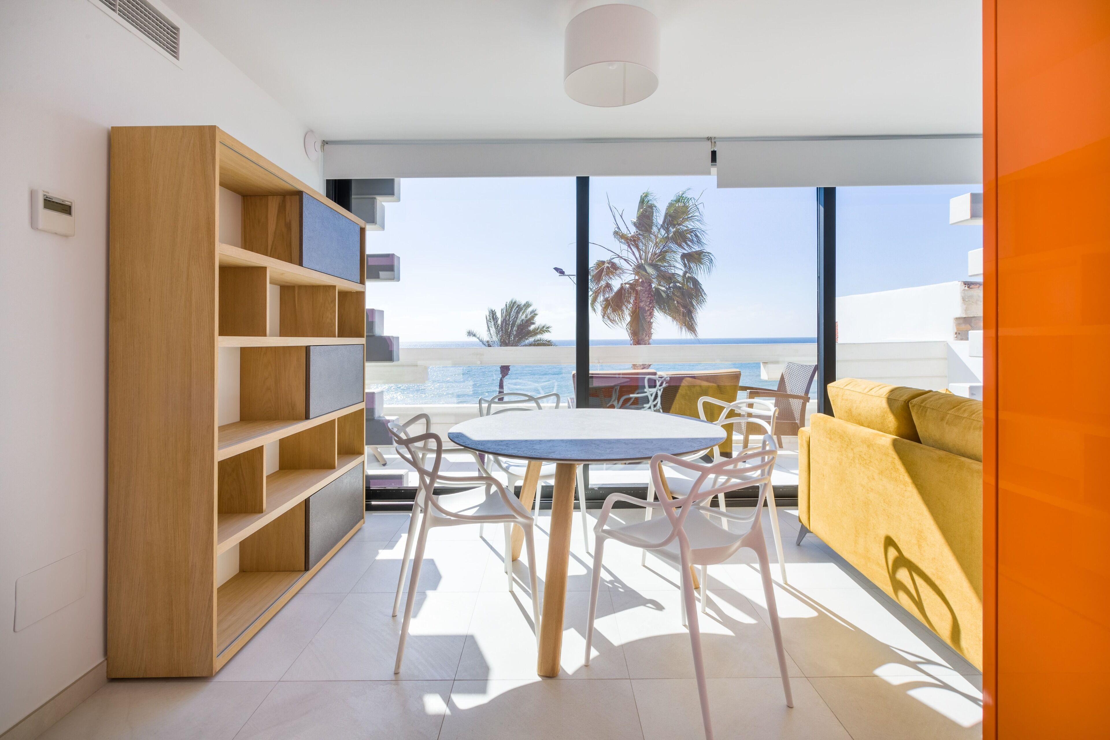 Un salon moderne avec un coin repas, de grandes fenêtres donnant sur la plage et un canapé jaune.
