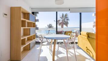 Un salon moderne avec un coin repas, de grandes fenêtres donnant sur la plage et un canapé jaune.