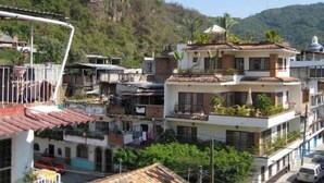 Un edificio residencial de varios pisos con balcones, rodeado de vegetación y colinas.